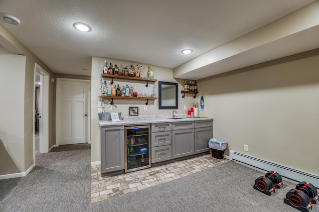 bar with baseboard heating, gray cabinets, a textured ceiling, beverage cooler, and light carpet