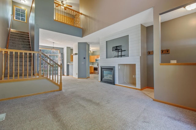 unfurnished living room featuring a fireplace, ceiling fan, a towering ceiling, and light colored carpet