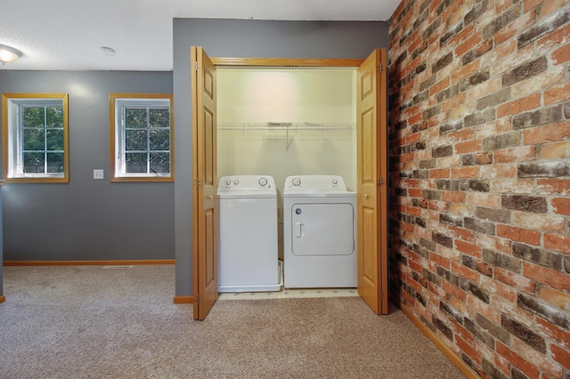 washroom featuring light carpet, brick wall, and washer and clothes dryer