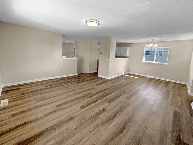 unfurnished living room with wood-type flooring, a textured ceiling, and a chandelier