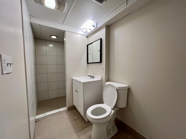 bathroom with a tile shower, vanity, toilet, and tile patterned floors