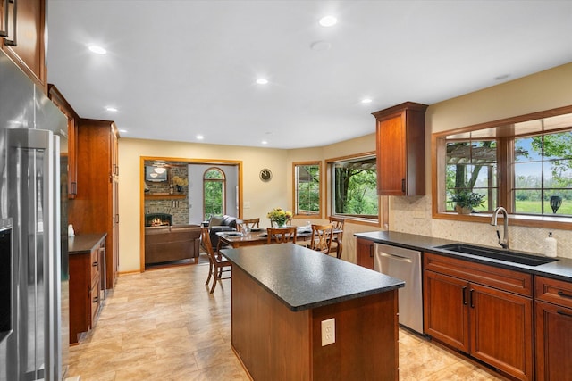 kitchen with a center island, sink, decorative backsplash, a stone fireplace, and stainless steel dishwasher