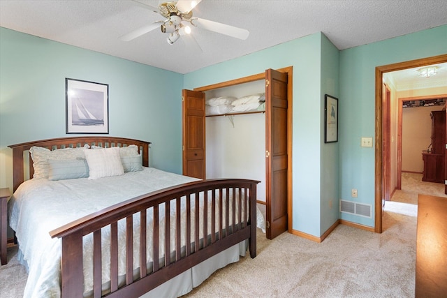 bedroom with a closet, ceiling fan, light colored carpet, and a textured ceiling