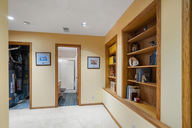 hall with dark carpet, a textured ceiling, water heater, and built in shelves