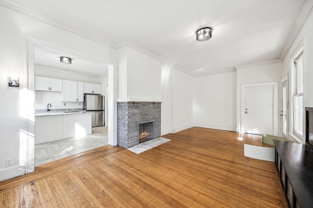 unfurnished living room with light wood-type flooring, crown molding, and a brick fireplace