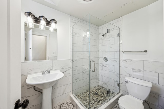 bathroom featuring tile walls, toilet, and a shower with shower door