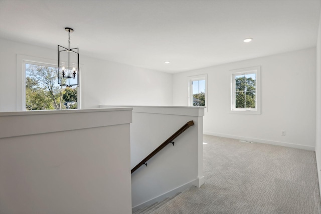 hall with a wealth of natural light, light carpet, and an inviting chandelier