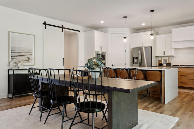 kitchen featuring a center island, hanging light fixtures, stainless steel appliances, a barn door, and white cabinets