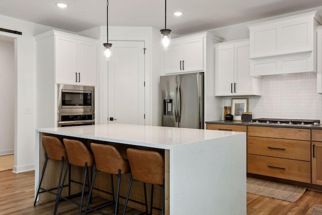 kitchen with stainless steel appliances, white cabinetry, hanging light fixtures, and a kitchen island