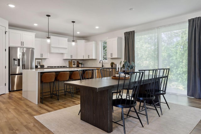 kitchen with stainless steel refrigerator with ice dispenser, a kitchen breakfast bar, white cabinets, a center island, and hanging light fixtures