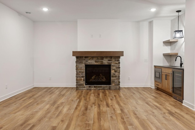 unfurnished living room featuring a stone fireplace, sink, beverage cooler, and light wood-type flooring