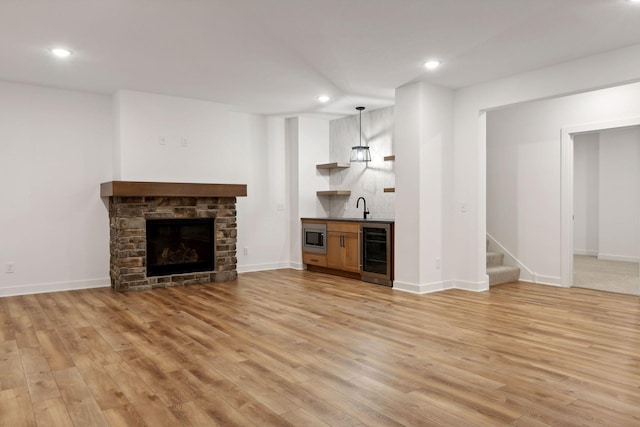 unfurnished living room with indoor wet bar, light hardwood / wood-style flooring, wine cooler, and a stone fireplace