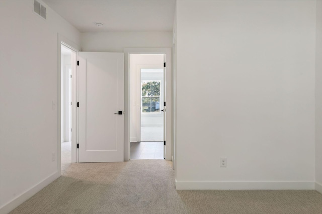 corridor with baseboards, visible vents, and light colored carpet