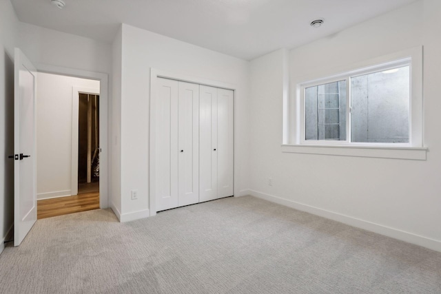 unfurnished bedroom with a closet, light colored carpet, and baseboards