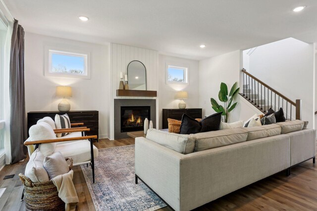 living room featuring recessed lighting, dark wood-style flooring, a large fireplace, and stairs