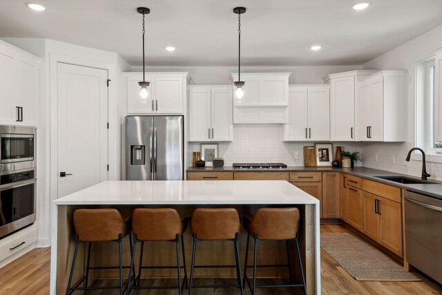 kitchen with a sink, white cabinetry, appliances with stainless steel finishes, brown cabinetry, and pendant lighting