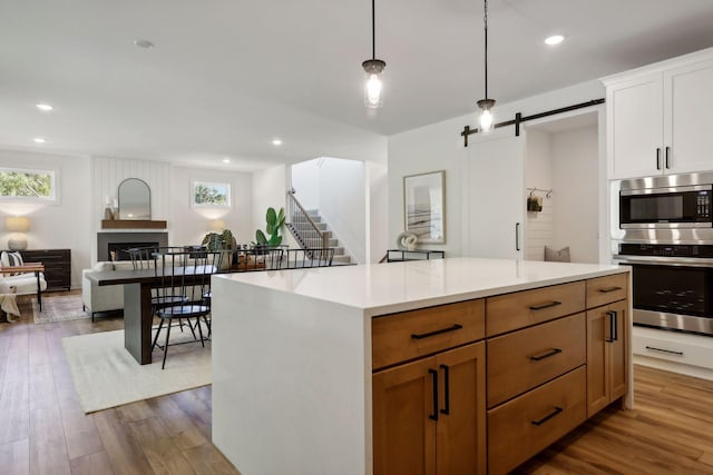 kitchen with a barn door, brown cabinets, open floor plan, stainless steel appliances, and light countertops