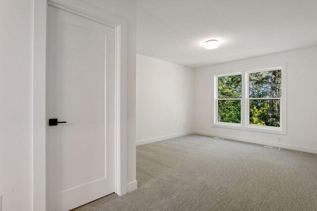 spare room featuring light colored carpet, visible vents, and baseboards