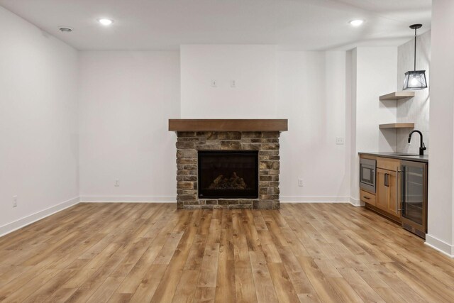 unfurnished living room with light wood-style floors, wine cooler, baseboards, and a stone fireplace