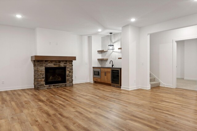 unfurnished living room with wine cooler, a fireplace, a sink, light wood-type flooring, and indoor wet bar