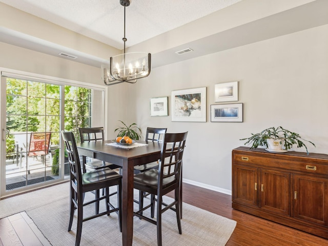 dining space with dark wood-type flooring, a textured ceiling, and an inviting chandelier