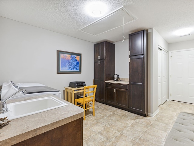 kitchen featuring dark brown cabinets, a textured ceiling, washing machine and dryer, and sink