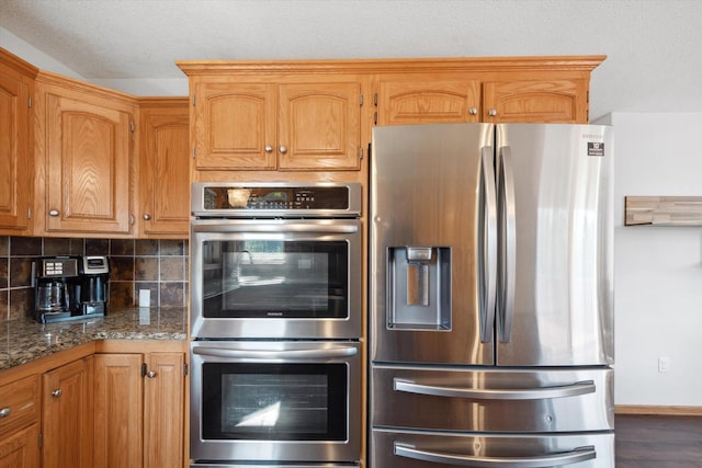 kitchen featuring a textured ceiling, decorative backsplash, stainless steel appliances, and stone counters