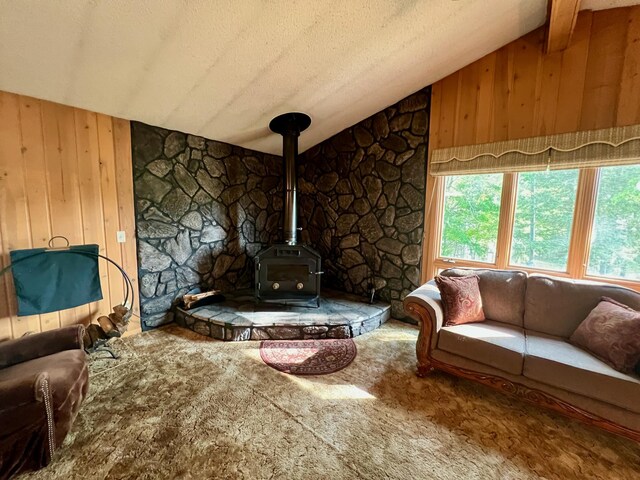 living room with carpet, wood walls, a wood stove, a textured ceiling, and vaulted ceiling with beams