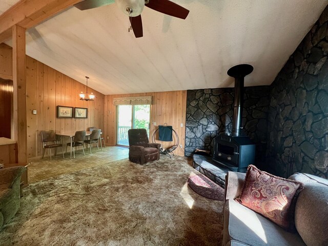 living room featuring ceiling fan with notable chandelier, a wood stove, lofted ceiling, and wooden walls