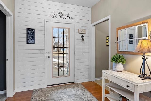 entryway featuring baseboards, wooden walls, and wood finished floors