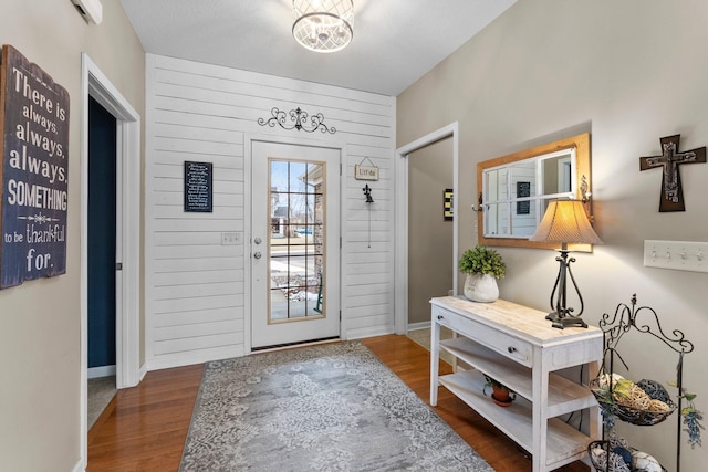 entryway with baseboards, a notable chandelier, wood finished floors, and wood walls