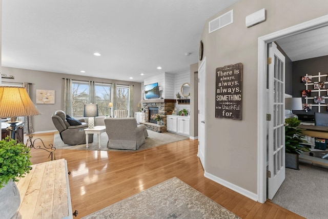 living room with a stone fireplace, recessed lighting, visible vents, and light wood-type flooring