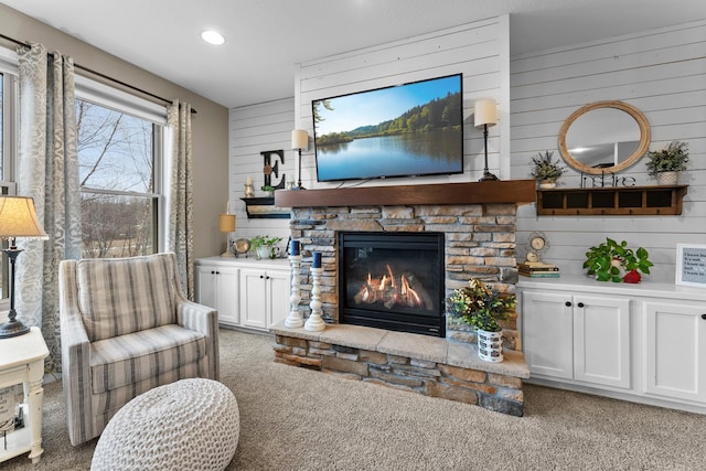 living area with recessed lighting, light colored carpet, a stone fireplace, and wooden walls