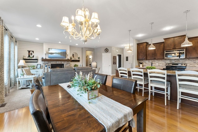 dining room featuring a stone fireplace, recessed lighting, light wood-style floors, and a chandelier