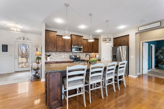 kitchen with tasteful backsplash, dark brown cabinetry, a breakfast bar, light wood-type flooring, and stainless steel appliances