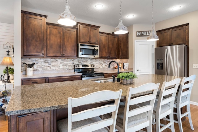 kitchen featuring light wood-type flooring, a sink, tasteful backsplash, dark brown cabinetry, and appliances with stainless steel finishes