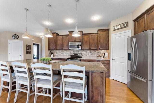 kitchen featuring a center island with sink, light wood finished floors, a sink, appliances with stainless steel finishes, and tasteful backsplash