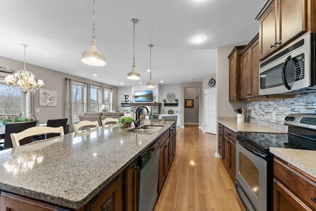 kitchen with a kitchen island with sink, a sink, backsplash, appliances with stainless steel finishes, and light wood finished floors