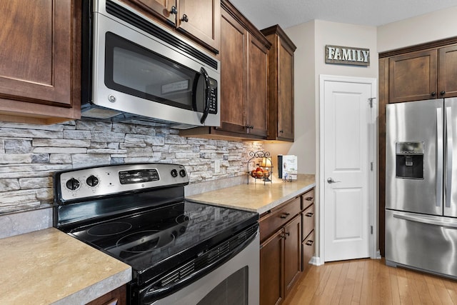 kitchen with light wood-style flooring, light countertops, dark brown cabinets, appliances with stainless steel finishes, and backsplash