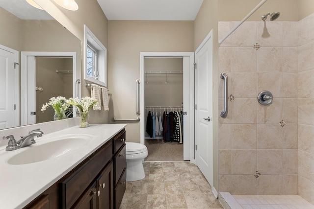 bathroom with a tile shower, toilet, vanity, and a walk in closet