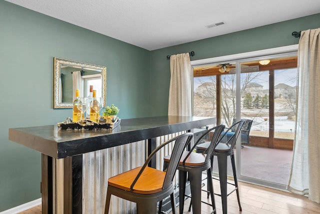 dining area with light wood finished floors, visible vents, baseboards, ceiling fan, and a bar