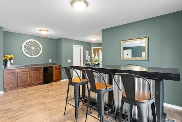 bar with baseboards, light wood-style floors, refrigerator, and a textured ceiling