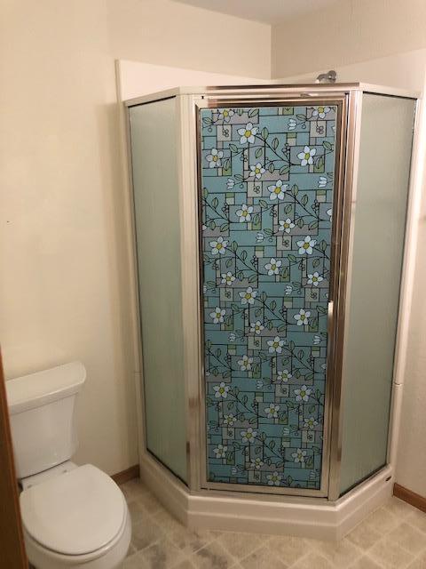 bathroom featuring a shower with door and toilet