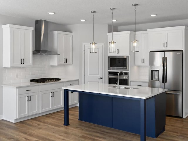 kitchen featuring wall chimney range hood, an island with sink, white cabinets, and appliances with stainless steel finishes