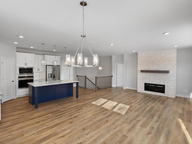 kitchen featuring a kitchen island with sink, hanging light fixtures, white cabinetry, stainless steel appliances, and light hardwood / wood-style floors