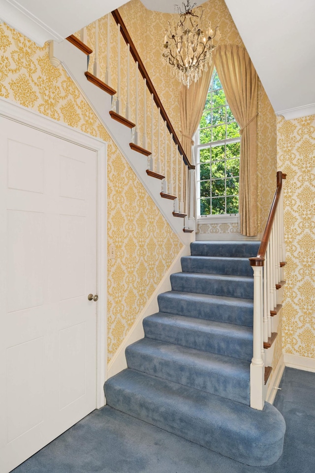 staircase with ornamental molding, carpet flooring, and an inviting chandelier