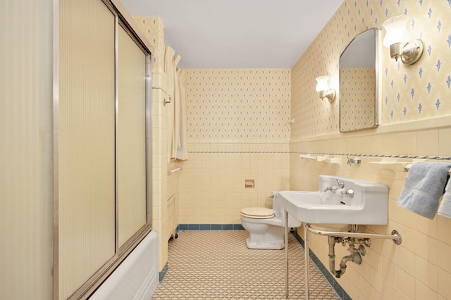 bathroom featuring toilet, tile patterned floors, tile walls, and shower / bath combination with glass door