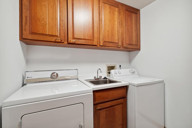 clothes washing area featuring cabinets, a textured ceiling, washing machine and clothes dryer, and sink