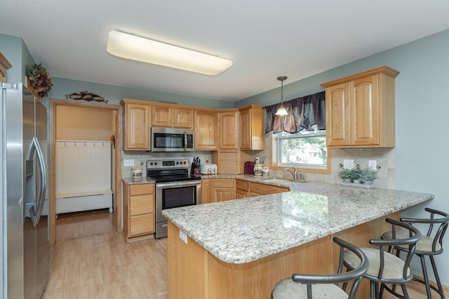 kitchen with kitchen peninsula, tasteful backsplash, a kitchen breakfast bar, appliances with stainless steel finishes, and light wood-type flooring