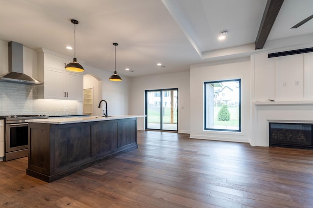 kitchen featuring a center island with sink, white cabinets, dark wood-type flooring, stainless steel range with gas stovetop, and wall chimney exhaust hood